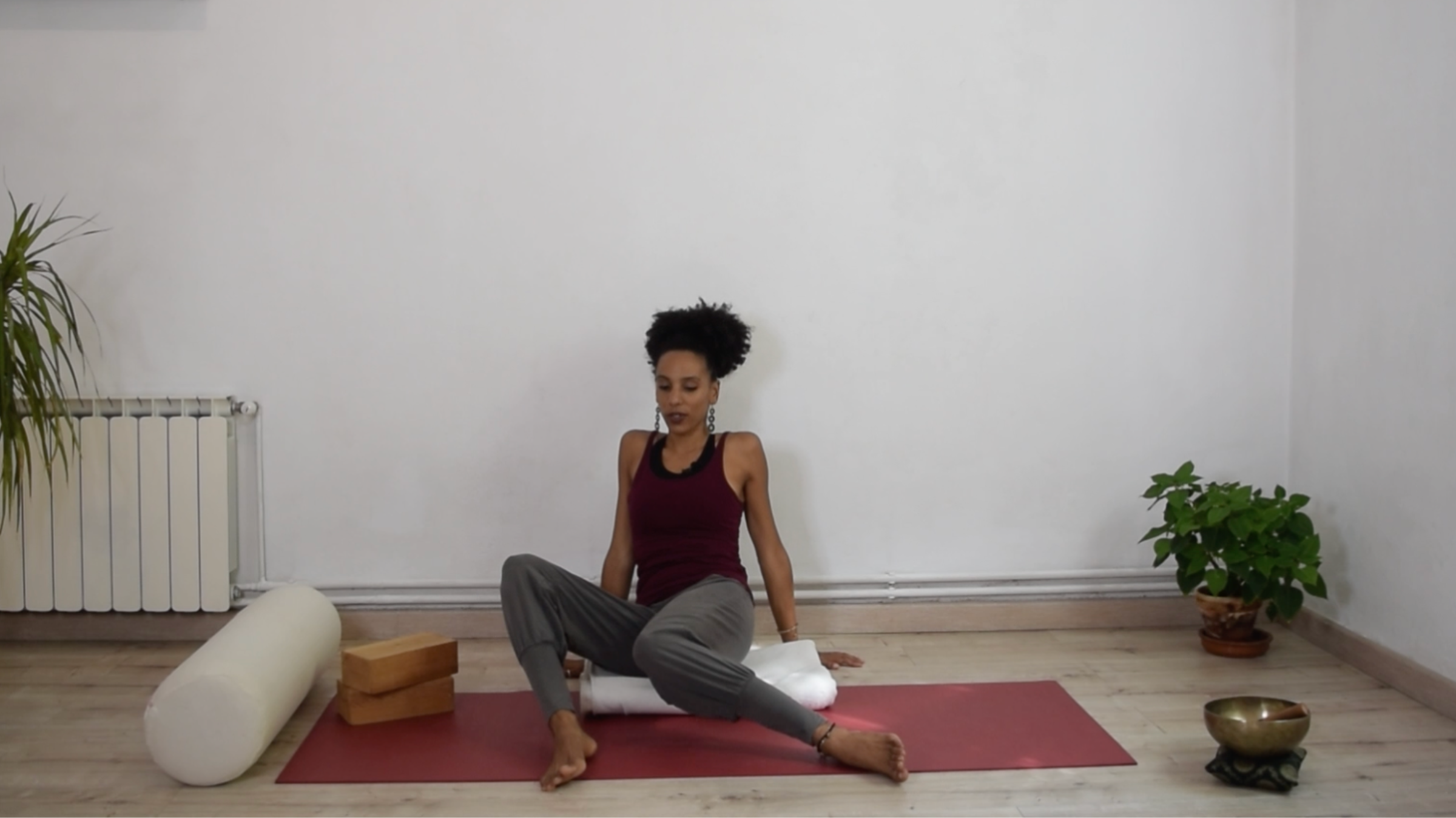 A practitioner seated on a yoga mat with knees bent and feet placed wide, lowering both knees simultaneously to one side.